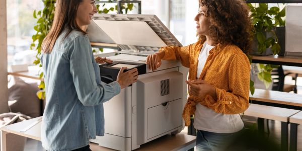 Two women talking by a photocopier in an office.