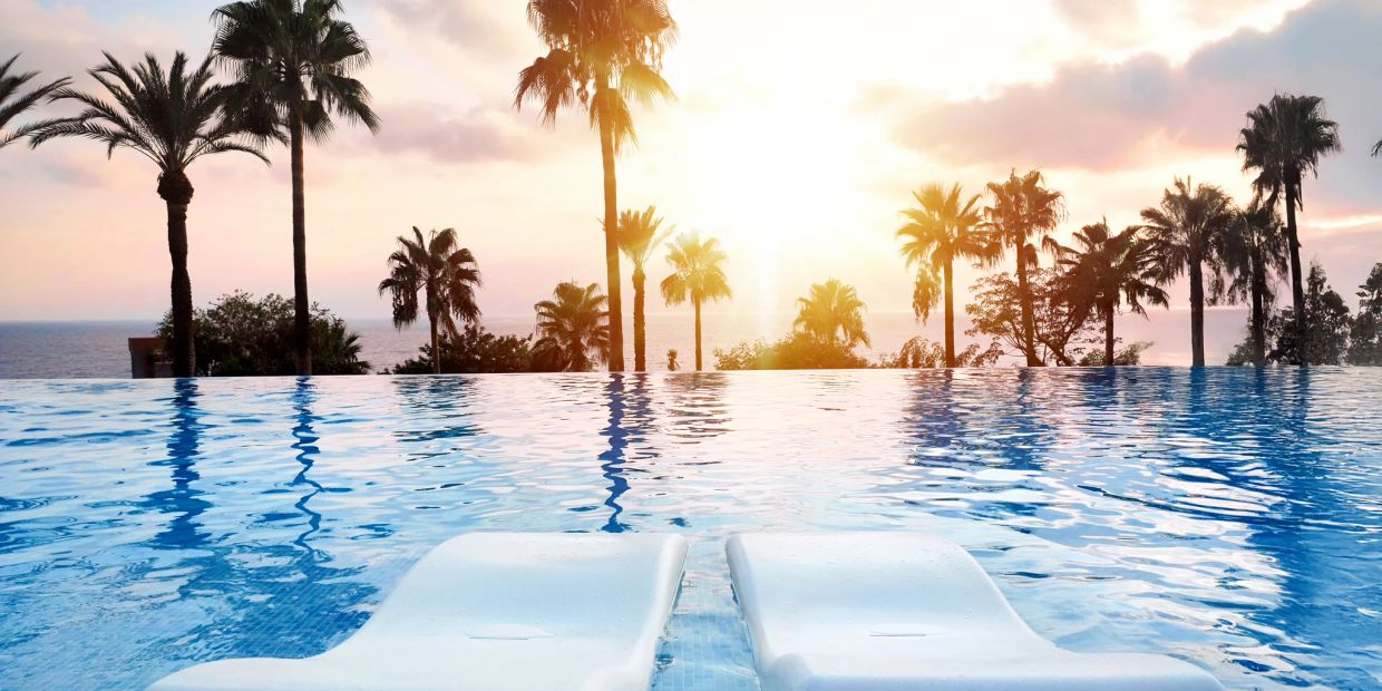 Sunset over infinity pool with palm trees.