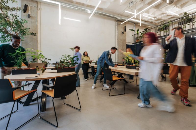 Diverse colleagues collaborating and moving around in a dynamic workspace filled with plants, showcasing a vibrant and productive atmosphere