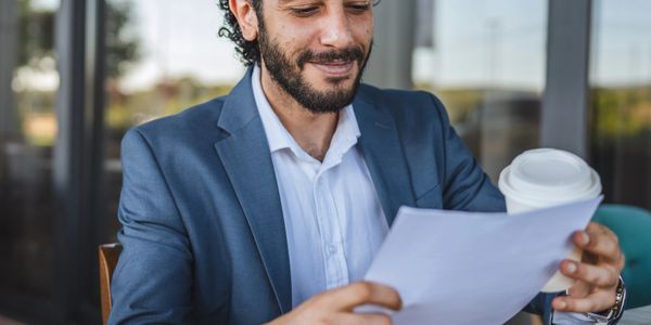Man in suit reading a document while holding a coffee cup.