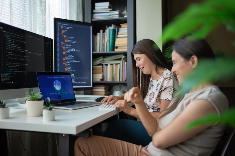 Two computer programmers focus on resolving IT issues, using multiple monitors & AI chatbot at office to analyze and develop solutions for customer. Multitasking, programming language development, technology & freelance job concept