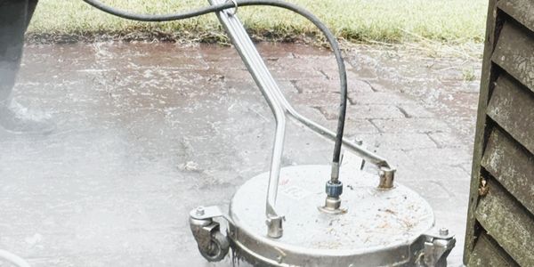 Surface cleaner attached to a pressure washer cleaning an outdoor patio.