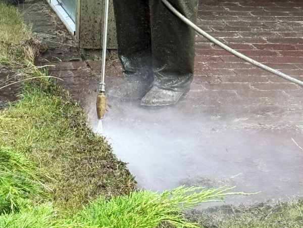 Person pressure washing a brick surface next to grass.