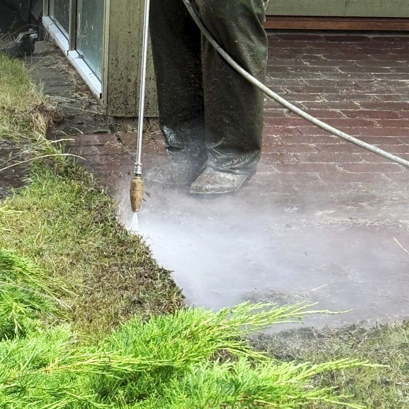 A person operating a high-pressure water cleaning machine on outdoor cement paving stones. The strong water jet removes dirt, algae, and weather stains, bringing the stone surface back to life. Concept of patio cleaning, outdoor maintenance, and surface restoration.