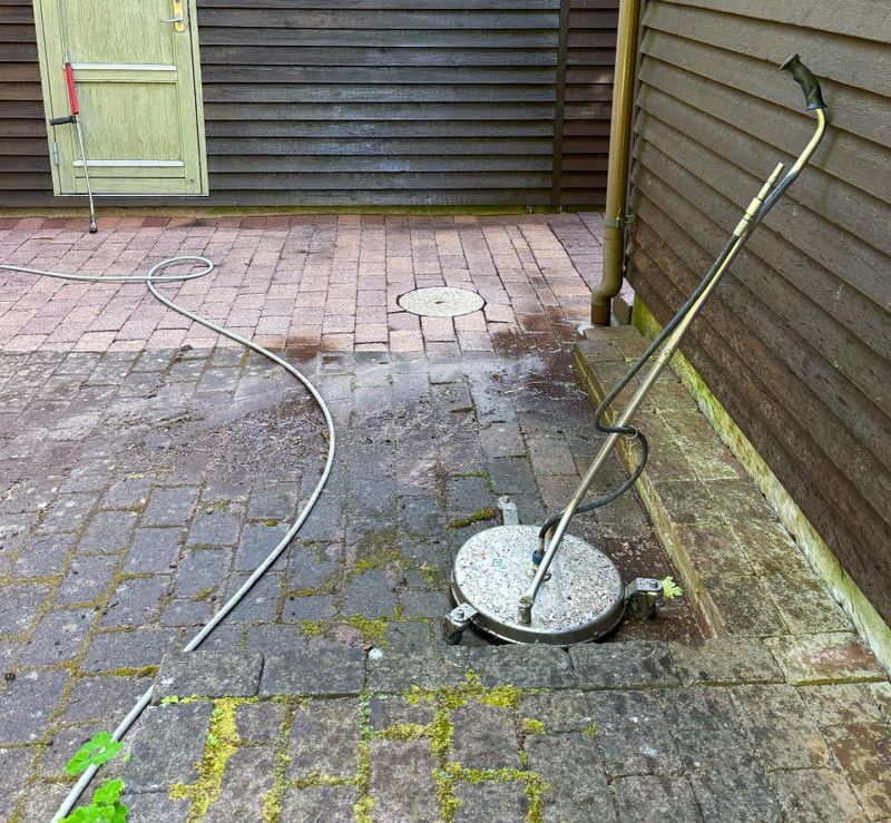 Close-up of a high-pressure washer in use, removing dirt, algae, moss, and lichen from old weathered cement paving slabs. Outdoor patio or driveway cleaning concept, showing restoration of concrete surfaces with powerful water jet equipment.