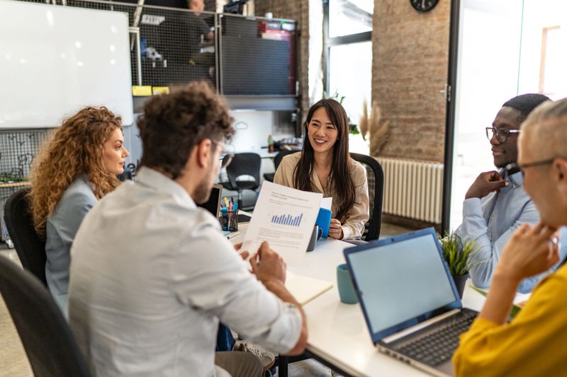 Diverse team of business professionals collaborating on financial reports, engaging in productive discussion and strategic planning in a contemporary office setting