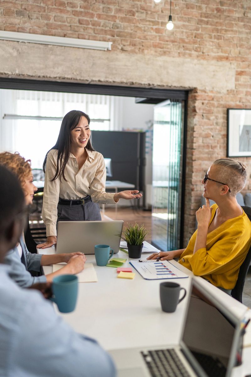 Smiling young asian businesswoman leads a productive meeting with her diverse team in a modern office, fostering collaboration and innovation