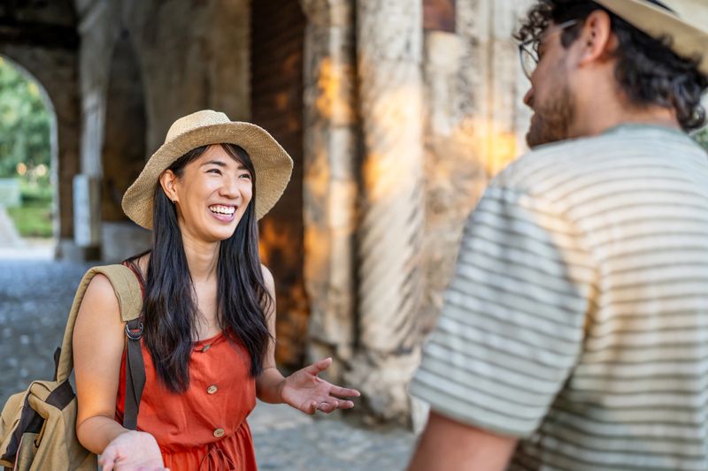 Two tourists wearing straw hats talking and smiling under an archway during their summer vacation