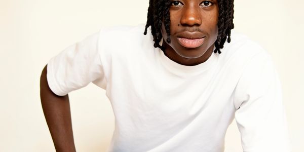 Young man with dreadlocks wearing a white t-shirt and blue jeans.