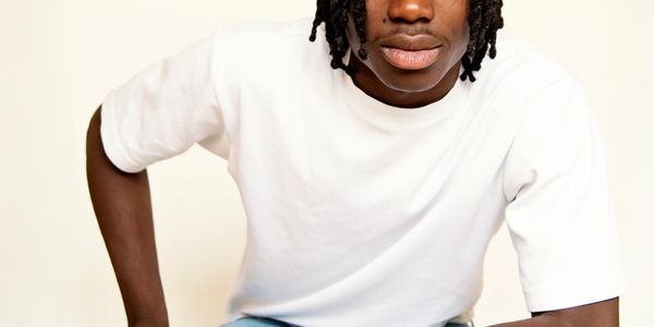 Young man with dreadlocks wearing a white t-shirt and blue jeans.
