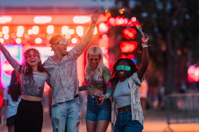 Four friends are dancing and having fun at an outdoor music festival, enjoying the vibrant atmosphere and live performances