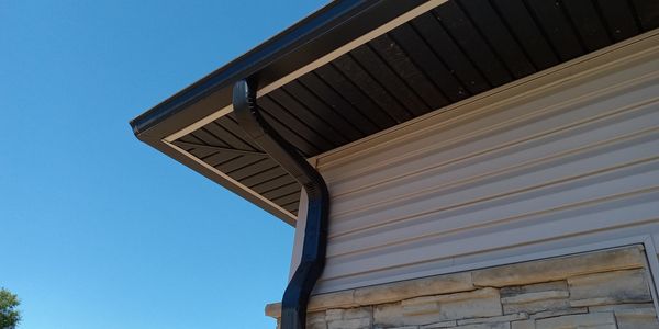Close-up of a house corner with a black gutter and clear blue sky.