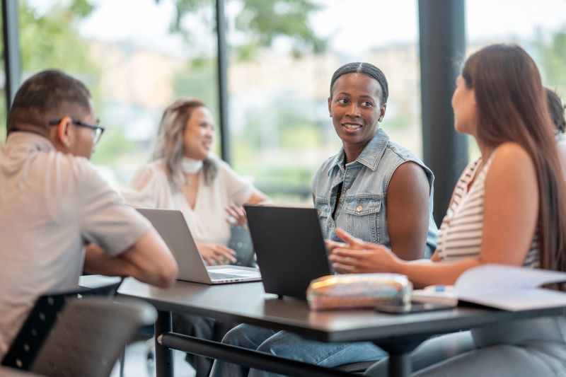 A group of individuals from varied backgrounds discussing ideas, working on laptops, and collaborating in a bright modern setting. The atmosphere reflects teamwork, diversity, and productivity.