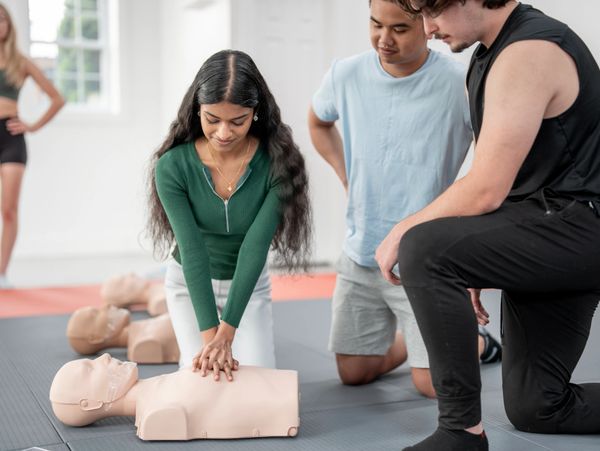 Person practicing CPR on a mannequin with defibrillator nearby.