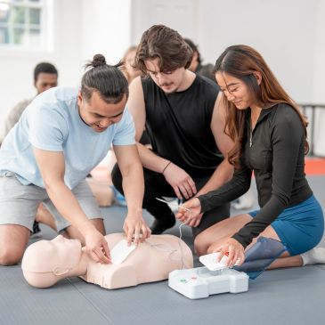 Group practicing CPR and defibrillator use on a mannequin.