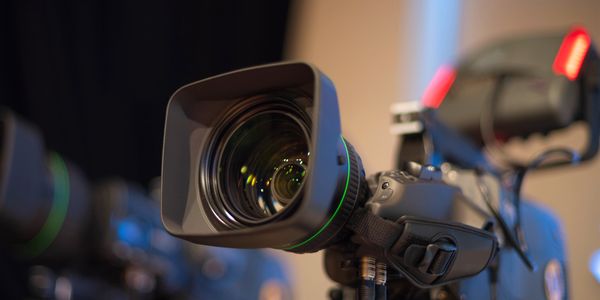 Close-up of a professional video camera lens with studio lights in the background.