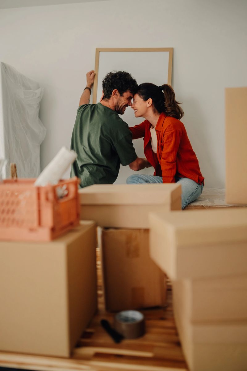 Young couple hanging a picture frame on the wall of their new apartment, surrounded by cardboard boxes