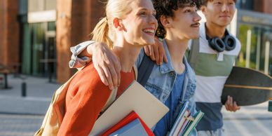 Three friends walking together with books and skateboard.