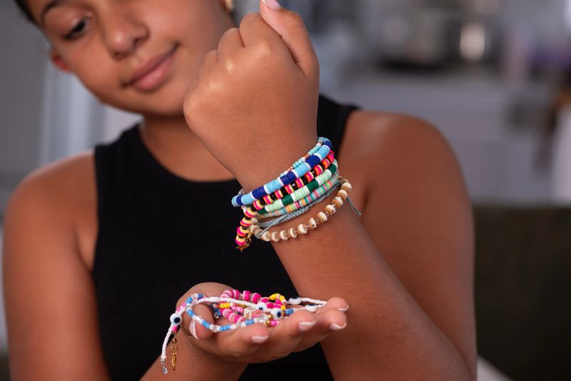 Close-up of a girl wearing multiple colorful handmade beaded bracelets on her wrist while holding more bracelets in her hand. The image highlights creativity, fashion accessories, handmade jewelry, and the joy of do-it-yourself crafting.