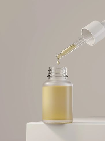 Dropper dispensing liquid into a frosted glass bottle.