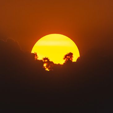 Bright yellow sun partially hidden by dark clouds during sunset.
