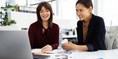 Two women working and smiling at a laptop.