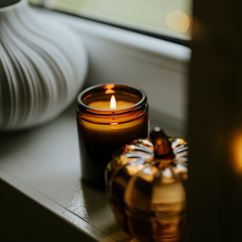 Still life on window sill with glass pumpkin and scented candle for autumn. Photo taken indoors