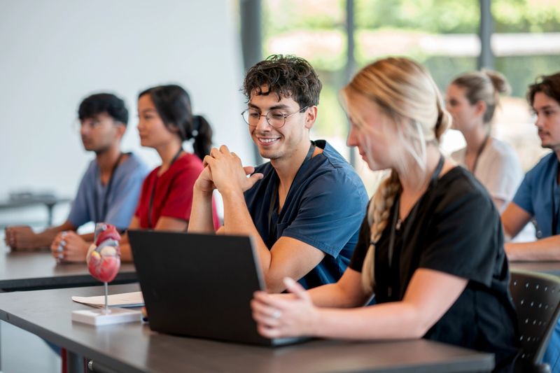 Diverse group of medical students engaging in collaborative learning at a university class, studying with digital devices and anatomical models. Scene emphasizes teamwork, academic focus, and professional preparation in the medical field.
