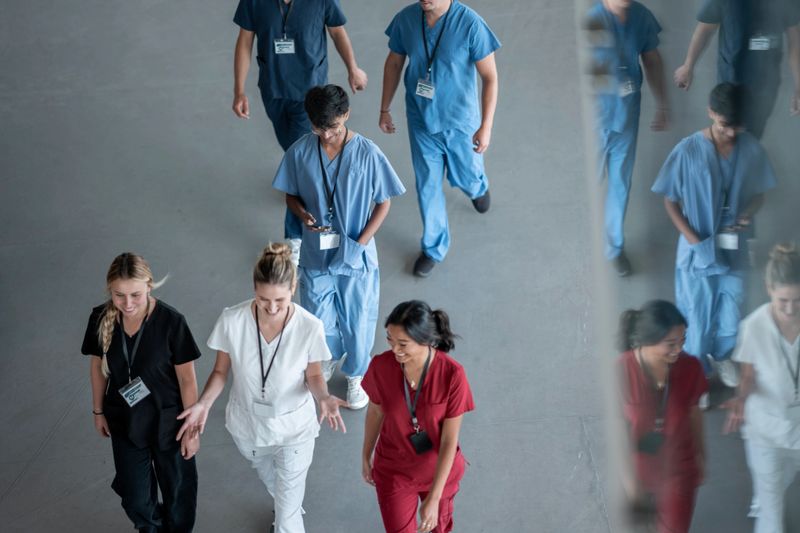 Diverse group of medical practitioners in scrubs and uniforms walking together in a hallway, showcasing teamwork and professional collaboration.
