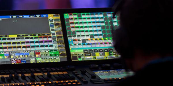 Person operating a complex lighting control console with colorful digital interface.