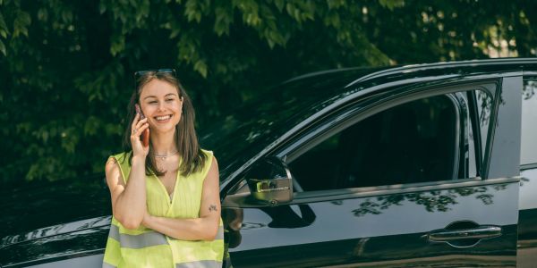 Woman in safety vest talking on the phone near a black car.