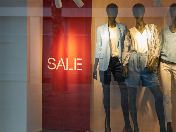 Store window display with mannequins and a sale sign.