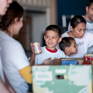 A young boy smiling while volunteering at a food bank.