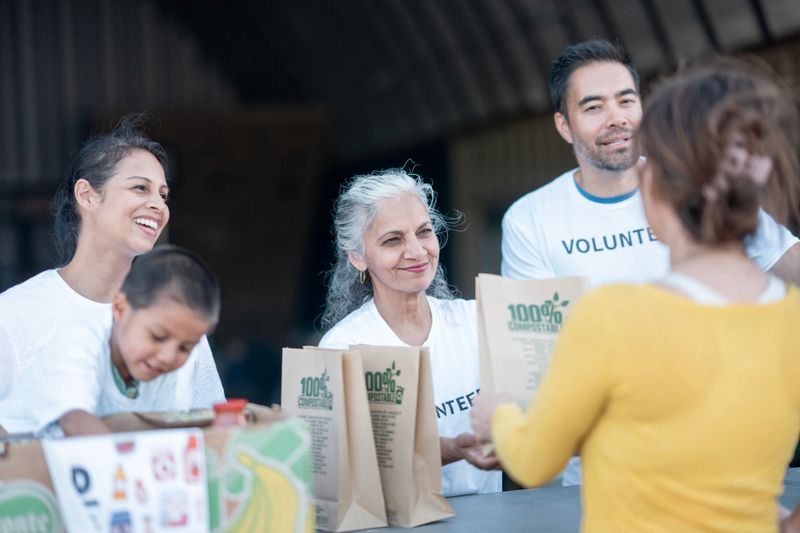 Group of compassionate volunteers giving out environmentally friendly food bags at a community aid center. Highlights diversity and teamwork.