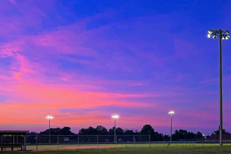 Blue and orange sunset over baseball field with field lights on