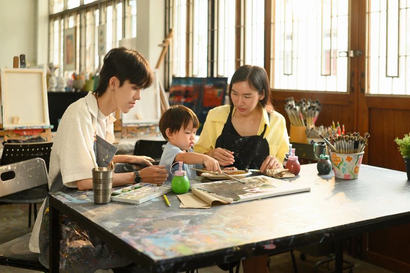 Little child enjoying painting with brush and palette in a hands-on learning art session. Family and teacher support enrich the creative experience.