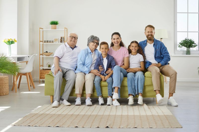 Big happy family sitting on sofa in cozy room. Portrait of grandparents, mother, father and their son and daughter posing together on coach at home and smiling at camera. Family spending time at home