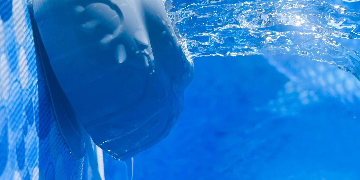 Water flowing from a decorative spout into a pool of clear blue water.
