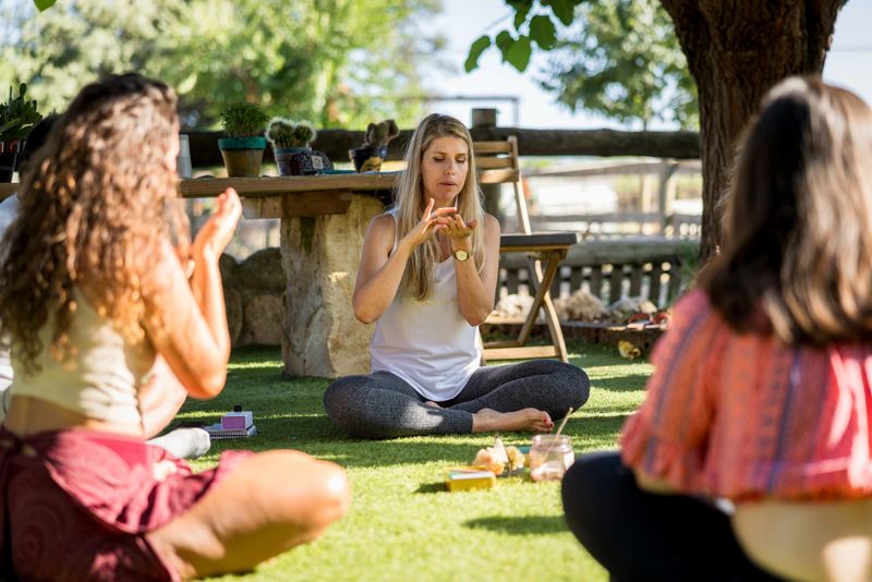 Group of women sitting in a circle on the grass, practicing systemic therapy with horses at a farm on a sunny summer day, fostering connection and personal growth through holistic healing. Smelling essential oil