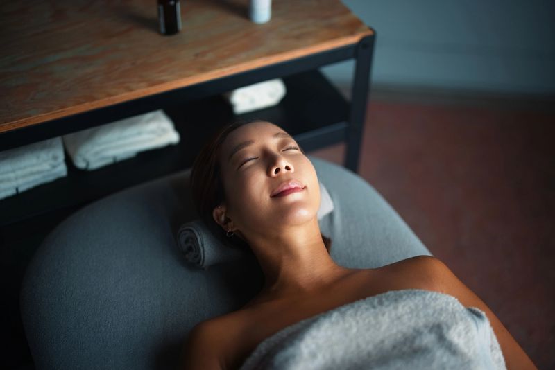 A serene depiction of a woman relaxing on a spa bed, draped in a towel, suggesting calm, tranquility, and indulgence in self-care in a professional wellness setting.