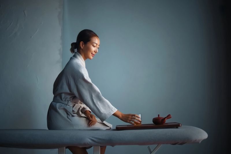 A serene scene of a woman in a robe enjoying a moment of tranquility with tea, showcasing peaceful relaxation and minimalist ambiance.