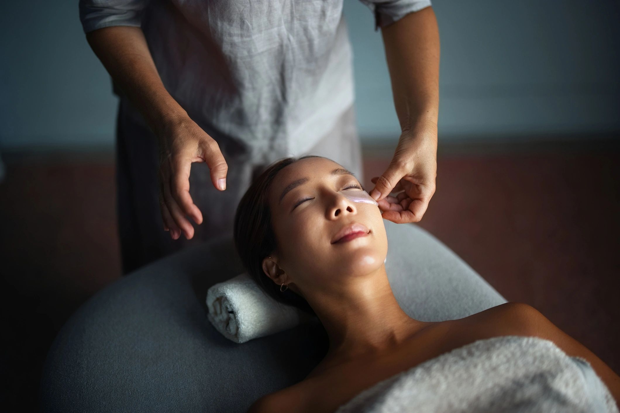 A woman enjoys a relaxing facial treatment with eye patches.