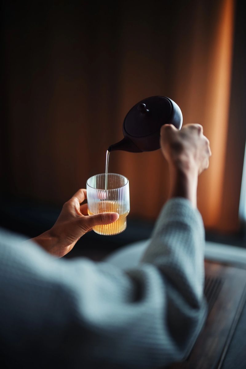 A close-up image showcasing a person pouring hot tea from a teapot into a glass cup, creating a warm and relaxing atmosphere.