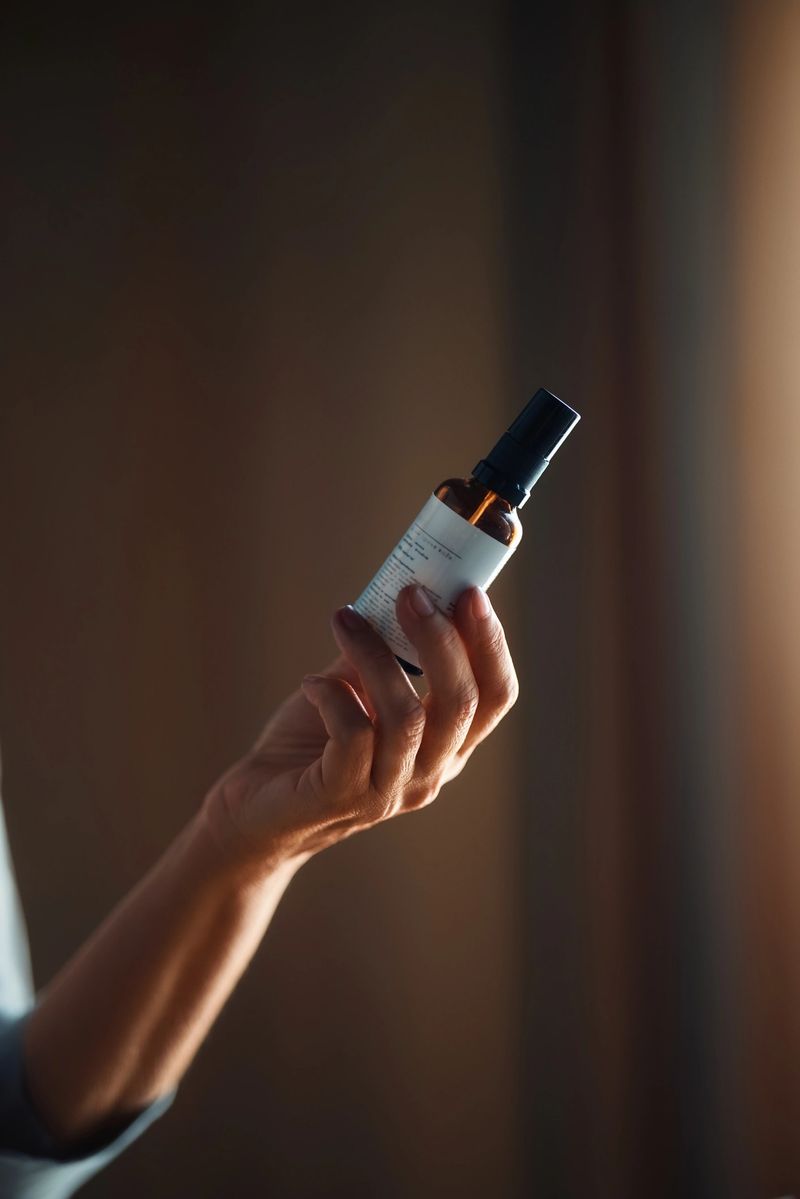 Close-up view of a hand holding a brown glass bottle with a spray nozzle, illuminated by warm ambient lighting that enhances the visual appeal and highlights its texture.