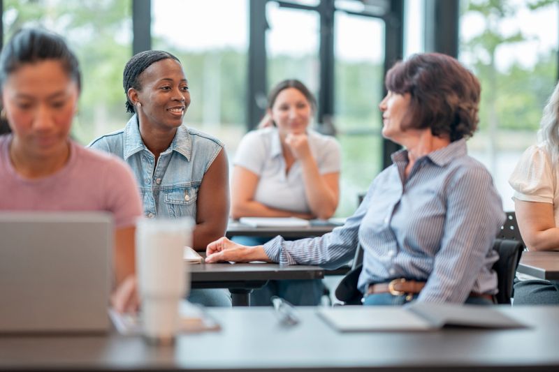 A group of diverse individuals interacts collaboratively engaging in a workshop, focusing on teamwork and camaraderie. The setting illustrates positive interpersonal relationships in a modern learning or professional environment.