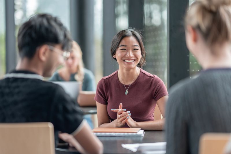 Smiling young students of diverse backgrounds working together in a group, fostering teamwork and shared learning during an educational study session. A setting that promotes collaboration, positivity, and academic engagement.