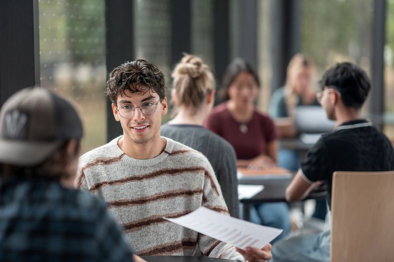 A diverse group of undergraduate students engaged in discussions and project work, fostering collaboration and creativity in a modern university environment. Ideal representation of academic teamwork and cultural inclusivity.