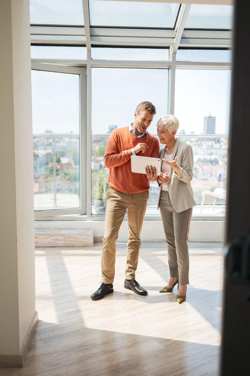 Professional colleagues having a discussion while holding a tablet in a sunlit office space. The setting creates a collaborative atmosphere, emphasizing teamwork, modern workplace dynamics, and technology-driven communication.