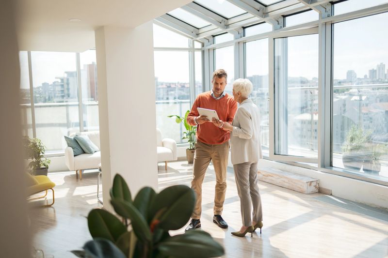 Two individuals collaborating in an open, contemporary office environment, reviewing important documentation together. Natural lighting from large windows creates a bright and welcoming ambiance for productive discussions.
