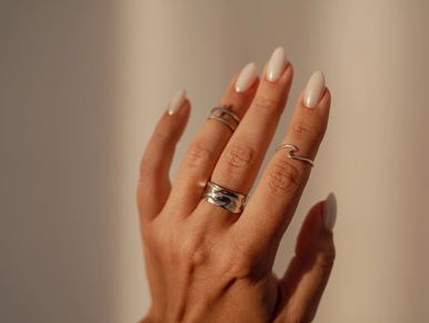 Hand with silver rings and nude nail polish.